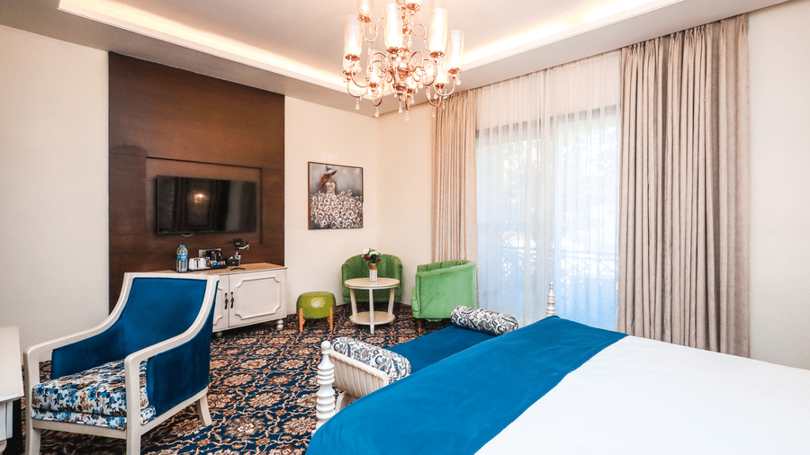Sitting area in a guest room at Estherea Resort & Spa, Jaipur with a blue armchair, a small green table, and light-coloured curtains.