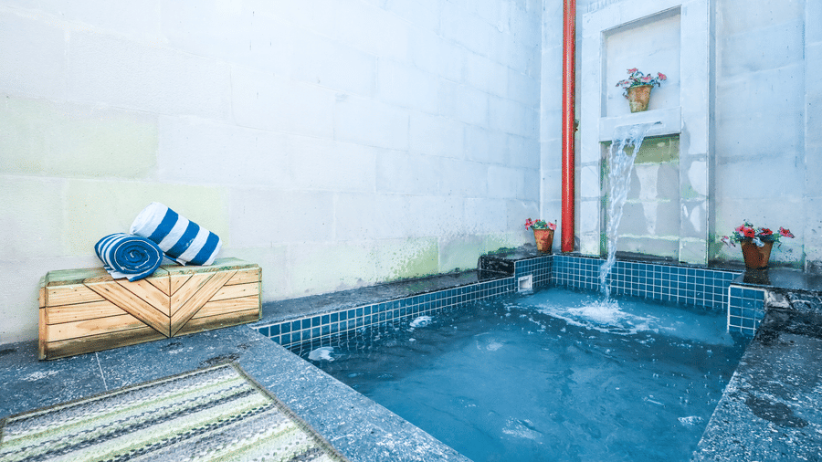 A private plunge pool at Estherea Resort & Spa, Jaipur with a stone waterfall feature, blue towels, and a striped mat on the deck.