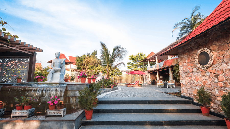 Wide stone steps leading toward a white statue and a resort building at Estherea Resort & Spa, Jaipur, under a clear blue sky.