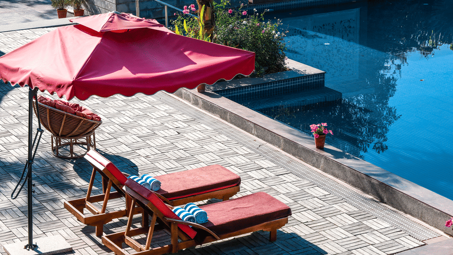 2 sun loungers with striped pillows under an umbrella on the paved pool deck at Estherea Resort & Spa, Jaipur.