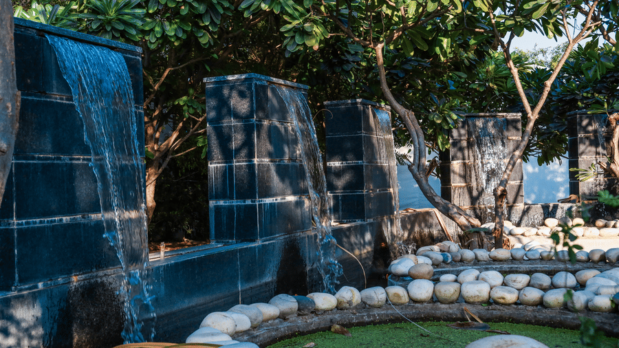 Detail of a stone water feature wall at Estherea Resort & Spa, Jaipur, with water cascading into a pond lined with white stones.