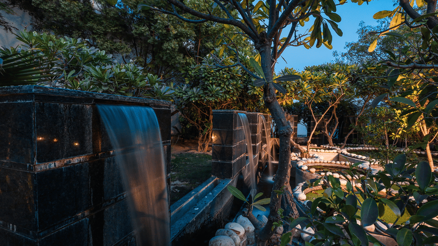 A water feature and surrounding greenery at Estherea Resort & Spa, Jaipur, showing reflections on the wet surfaces.