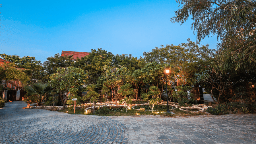 A paved driveway and landscaped garden at Estherea Resort & Spa, Jaipur, featuring lit trees and low-level stone-bordered ponds.