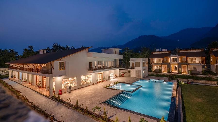 A resort with multiple buildings, a swimming pool, and a large lawn, illuminated at night against a backdrop of mountains.