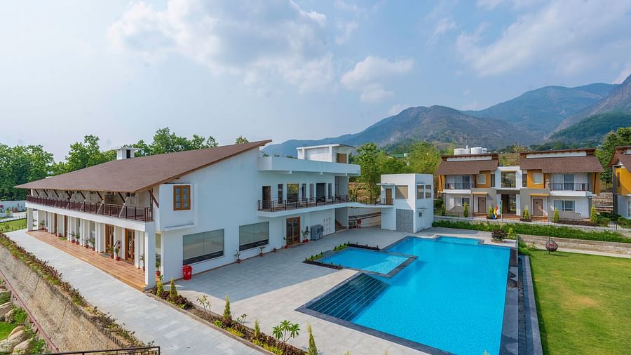 A resort with a large building, a swimming pool, and a lawn, surrounded by mountains.