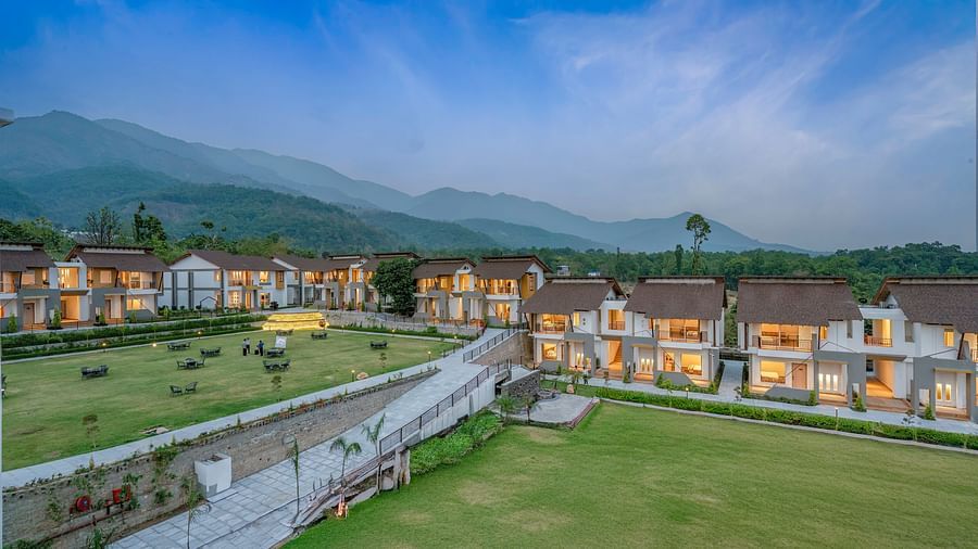 Shot of a resort with multiple buildings, a swimming pool, and a large lawn, surrounded by mountains.
