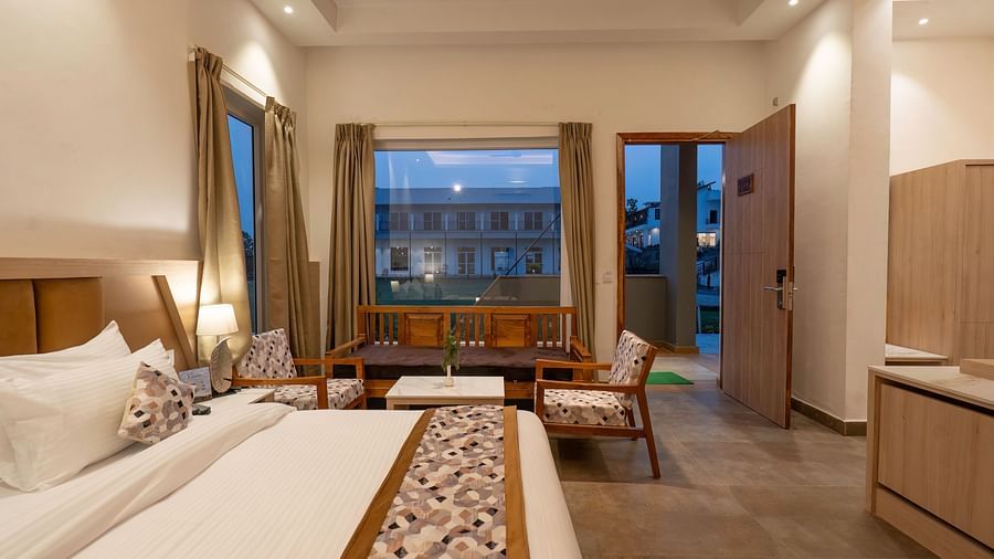 A modern hotel room with a king-size bed, a seating area, and a view of the lush green outdoors