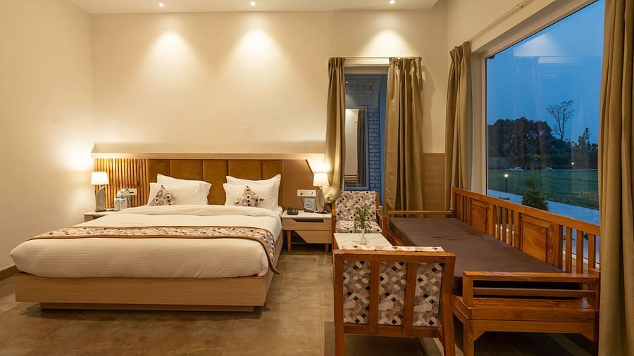 A cosy hotel room with a king-size bed, a seating area, and a view of the lush green outdoors.
