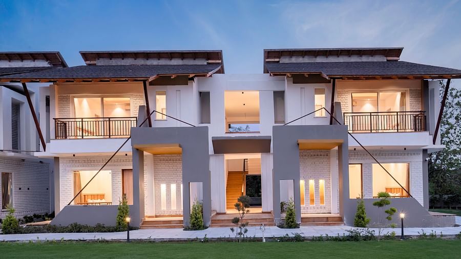 A modern villa with a balcony, surrounded by lush greenery and a clear blue sky.