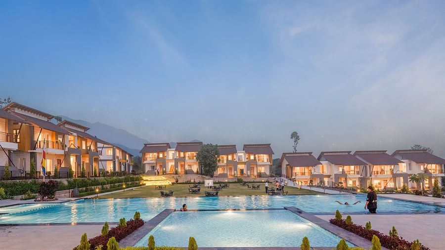 A large resort with multiple buildings, swimming pools, and fountains, illuminated at night.