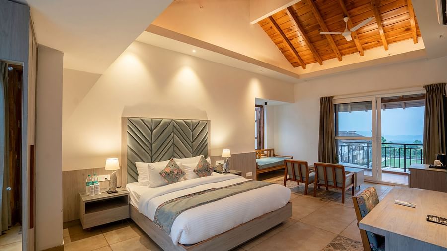 A modern hotel room with a king size bed, a seating area, and a view of the lush green outdoors.