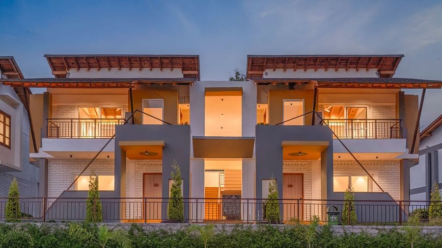 A modern villa with a balcony, surrounded by lush greenery and a clear blue sky.