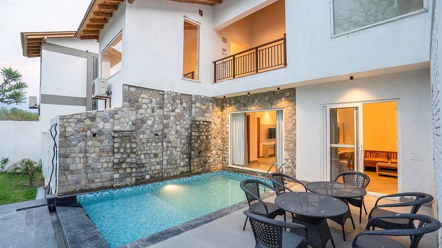 A shot of a vlla with a swimming pool and a patio, surrounded by lush greenery.