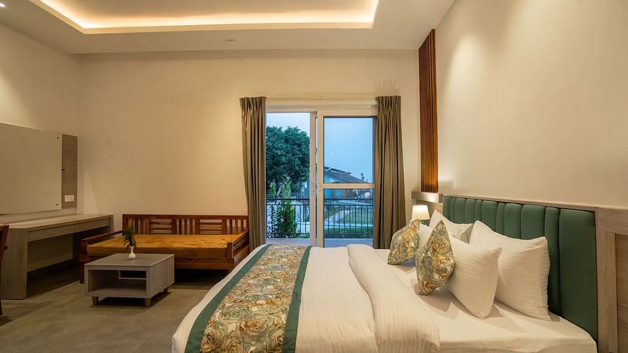 A modern hotel room with a king-size bed, a seating area, and a balcony offering a view of the lush green mountains.