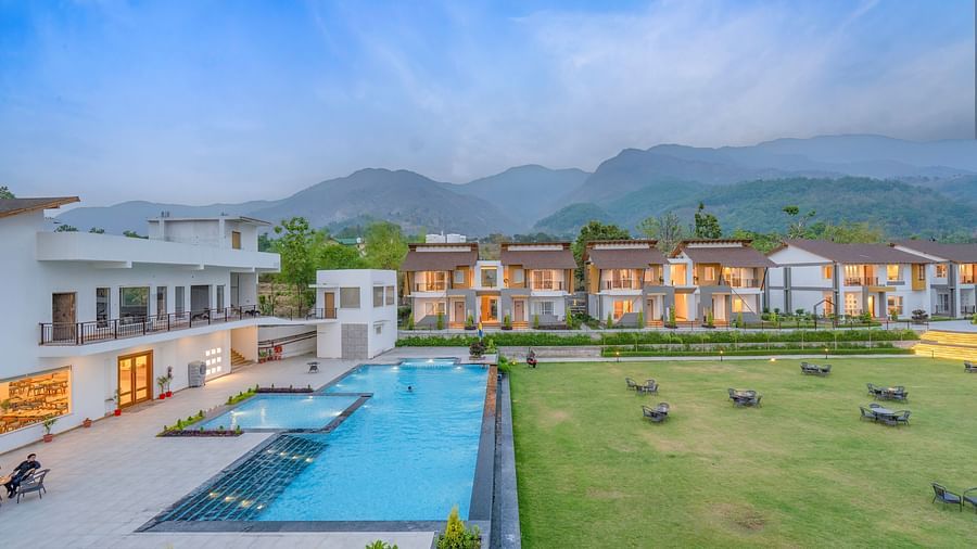 A picturesque resort nestled amidst rolling hills, featuring a sparkling swimming pool, lush green lawns, and a stunning mountain backdrop.