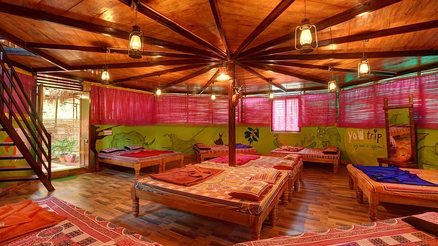 A wide angle image of wooden cottages with colourful beds and lanterns hanging from a high ceiling - Evergreen County