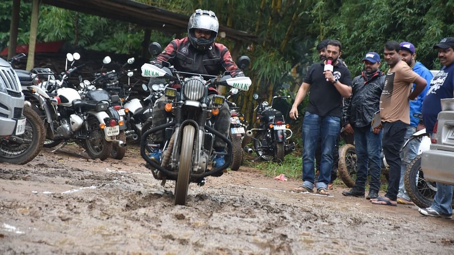 A person riding a bike on a muddy trail with people in the back looking at him - Evergreen County
