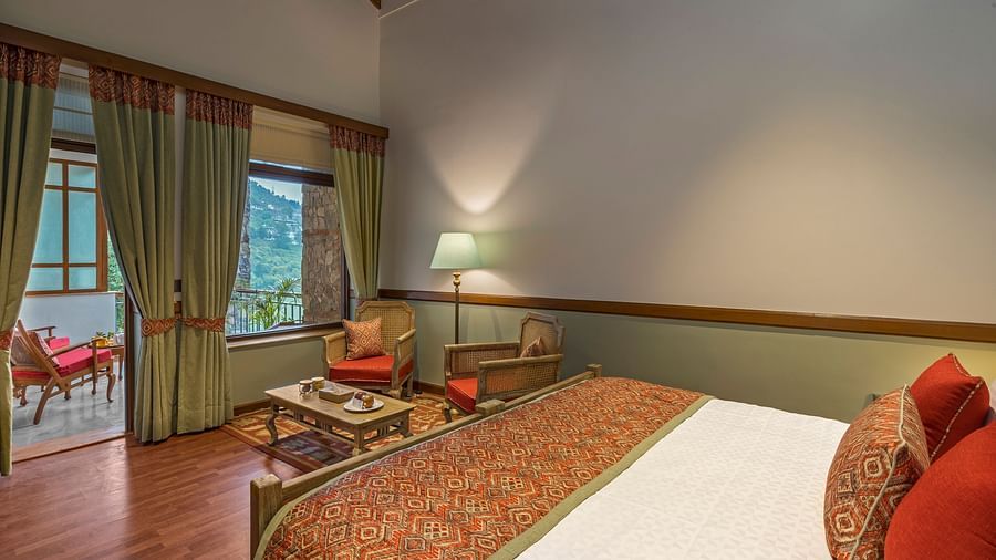 Top head view of Superior Rooms showcasing a cosy, royal interior with a comfortable bed, chair, and table, complemented by a beautiful hill view.