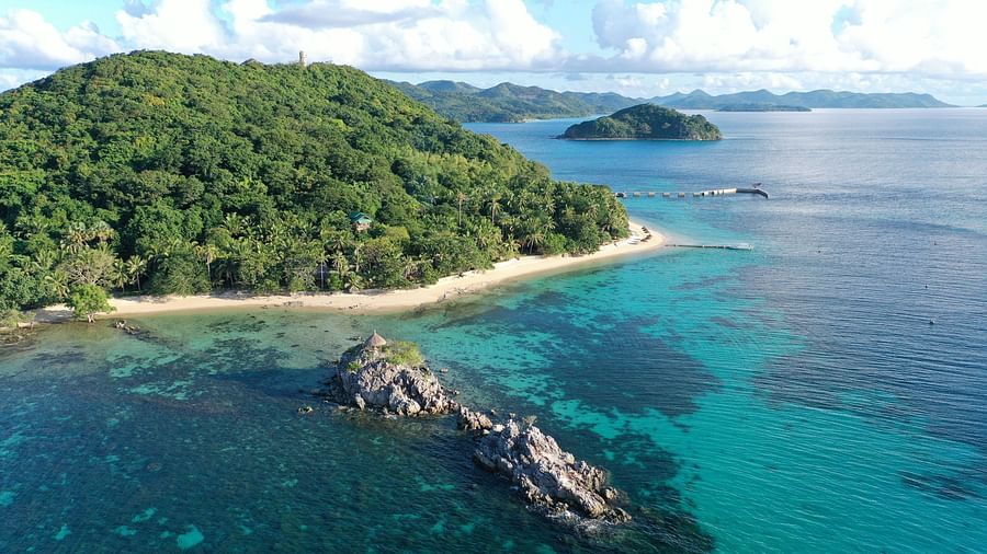 Aerial view of a lush green island surrounded by clear blue ocean and rocky coastline.
