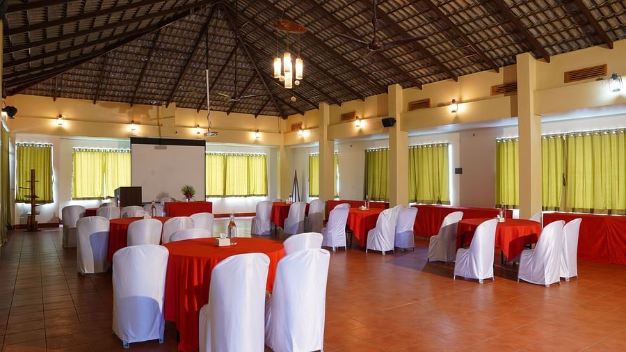 Another view of the banquet hall at Forest Escapes Koyna, showing rows of tables with red accents and white chairs.