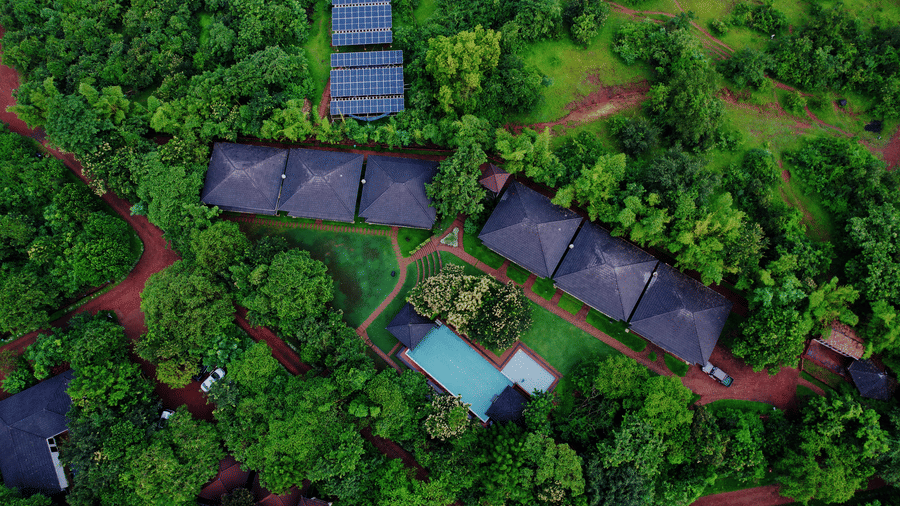 An aerial view of Forest Escapes, a nature resort near Pune, featuring cabins nestled in dense foliage, along with a swimming pool