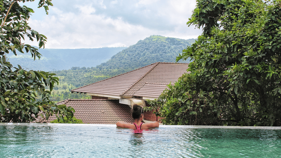 Guests at Forest Escapes Koyna relax in a swimming pool with a stunning view of the surrounding hills and greenery.