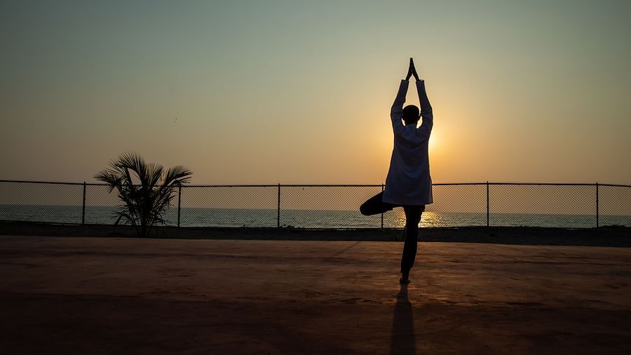 image of a person doing suryanamaskar standing on one leg with a sunrise in the background