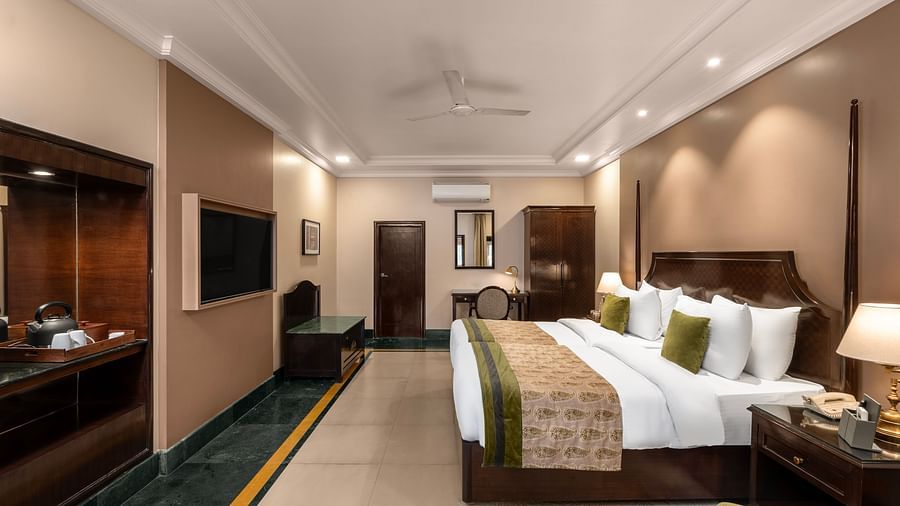Ganga View Room with a side drawer and side lamp, a workdesk and a large bed facing a television - Ganga Lahari, Haridwar