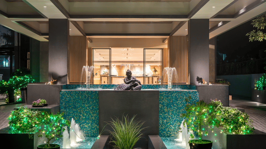 Illuminated entrance of Gemini Continental featuring a multi-tiered tile fountain with a Buddha statue and festive lights.