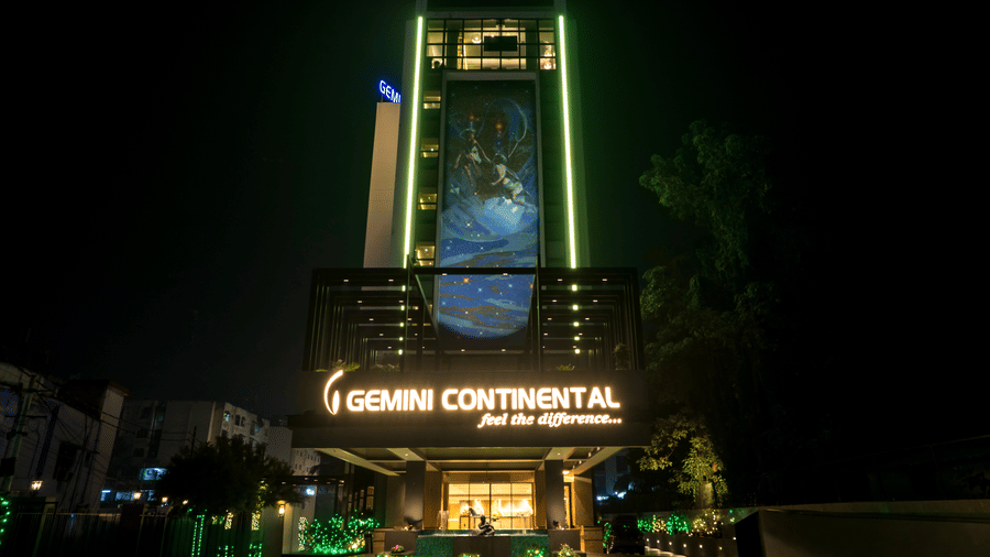 Facade view of the Gemini Continental hotel at night, featuring its illuminated name, a large decorative facade mural, and bright landscape lighting.