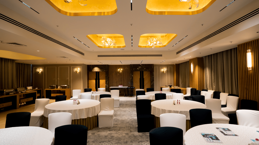 Banquet hall Galaxy 2 at Gemini Continental with round tables, tablecloths, black and white chairs, ceiling panels, hanging lights, chandeliers, carpeted floor, wall lights, curtains, and buffet tables.