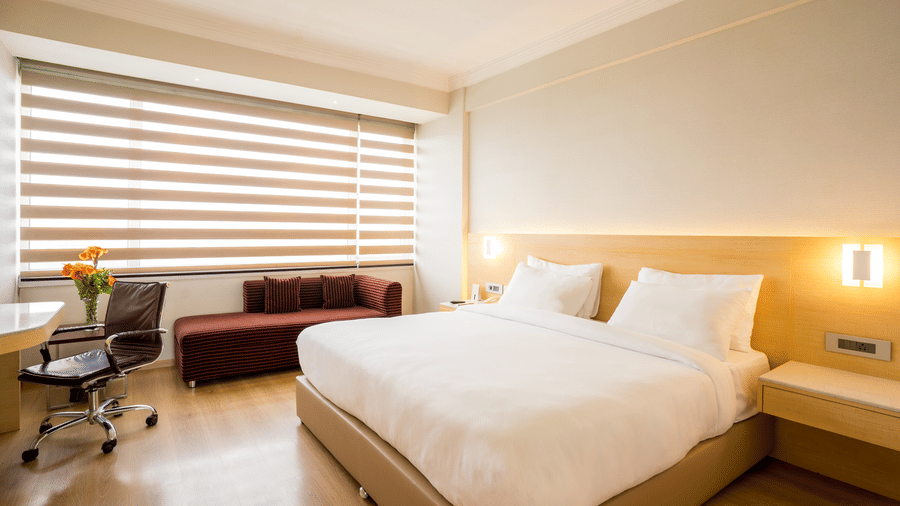 A Luxury Room at Gemini Continental with a plush bed, and a seating area with a sofa near a large window.