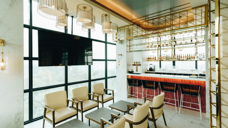 Modern interior of Seven Heaven Bar at Gemini Continental with armchairs, hanging lights, large windows, and a sleek bar lined with stools and bottles.