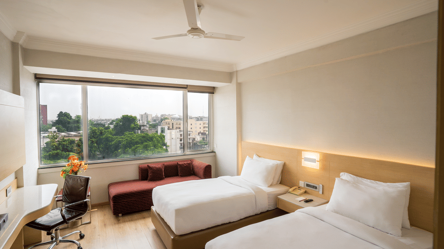 A Standard Room with twin beds, a large window, an office chair and a ceiling fan at Gemini Continental.