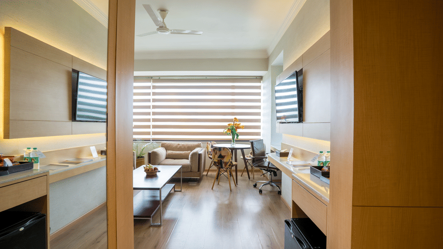 View into a Suite at Gemini Continental featuring a living area with a plush sofa, a dining table, a desk with an office chair, and a wall-mounted TV.