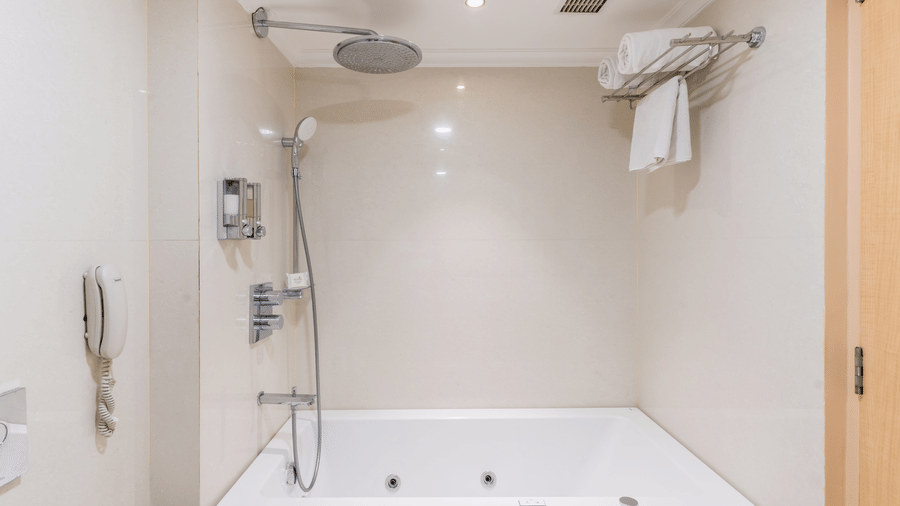 Bathroom of a Suite at Gemini Continental featuring a bath tub, an overhead shower, and bath towels neatly arranged on a metal shelf.