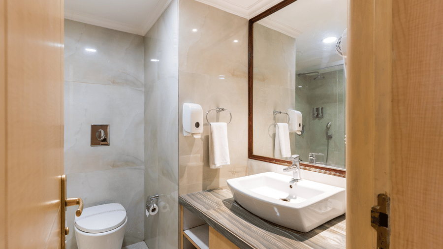 A hotel bathroom at Gemini Continental featuring a large wall mirror, a washbasin, tiled walls, and a western toilet.
