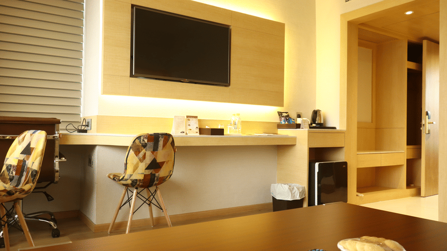 Suite living area with a wall-mounted television, a wooden work desk, chairs and a partly open door leading through to another room nearby.