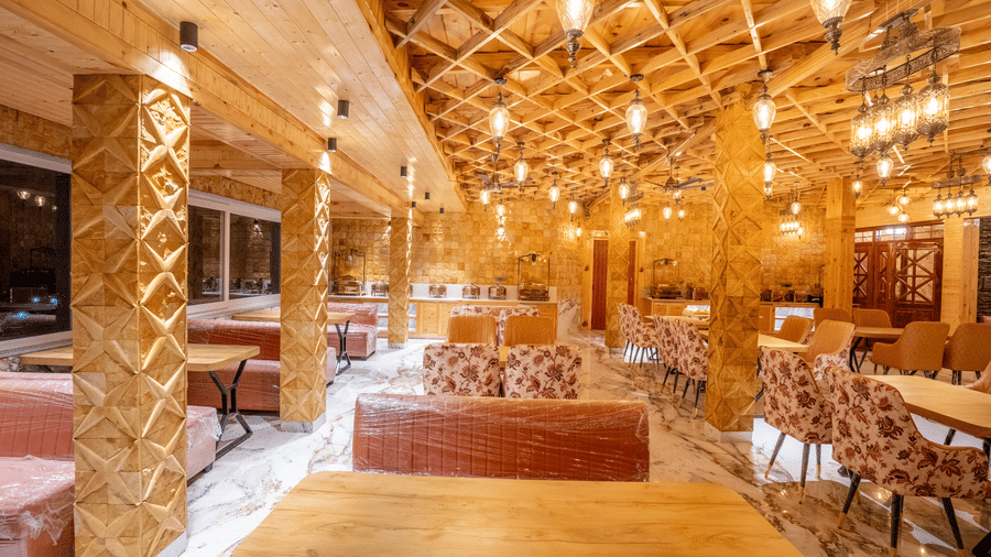 A grand dining hall with an intricate lattice wood ceiling, stone pillars, and warm hanging Edison bulbs - Golden Oak By The Lake Hill, Khurpatal