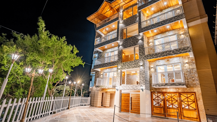 The multi-storey exterior of the hotel illuminated at night with warm golden lights - Golden Oak By The Lake Hill, Khurpatal