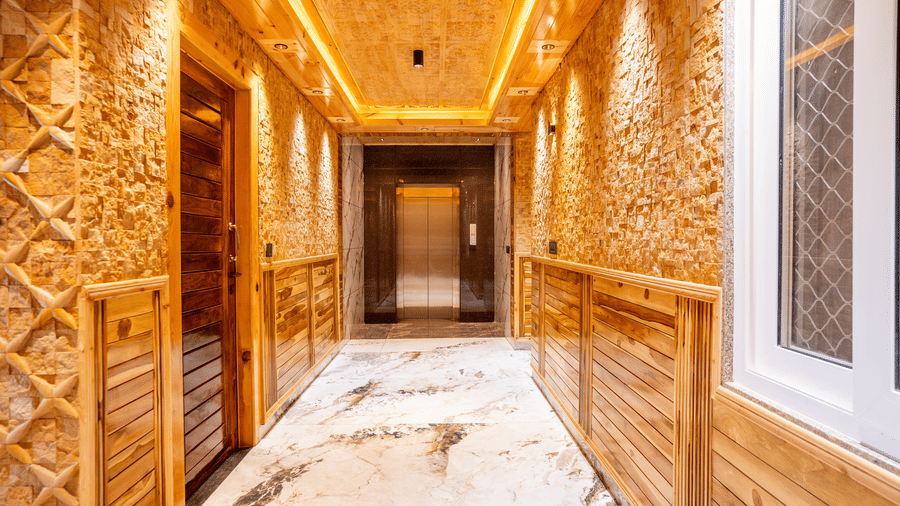 A brightly lit hotel hallway featuring marble floors, textured stone walls, and warm wood panelling - Golden Oak By The Lake Hill, Khurpatal