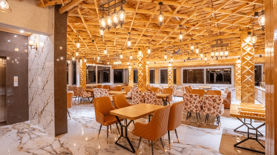 A well-lit restaurant area with marble flooring, wooden tables, and plush orange and floral chairs - Golden Oak By The Lake Hill, Khurpatal