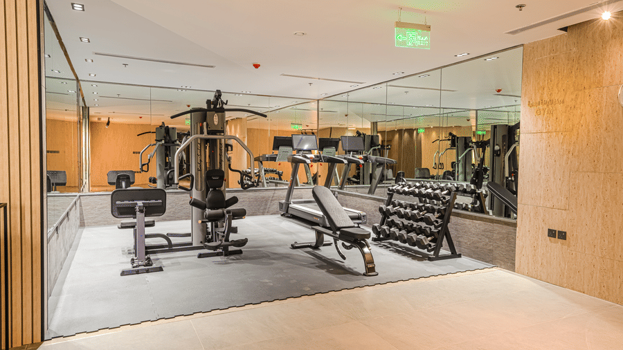 The indoor gym at Grand Iva Hotel, Abha, equipped with gym equipments for full body workouts, a mirror fit to cover the wall, and a carpet.