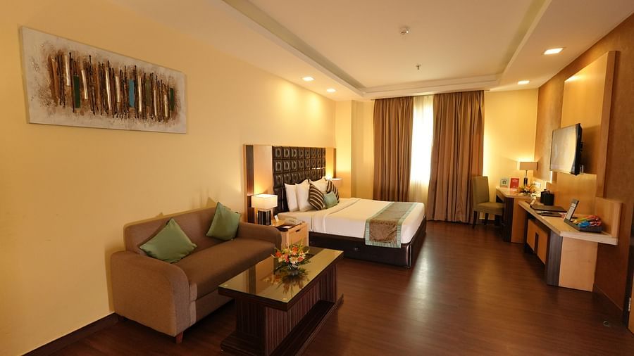Hotel suite featuring a bed, seating area, desk, and a large window with curtains - Grand Plaza Lords Inn Jammu