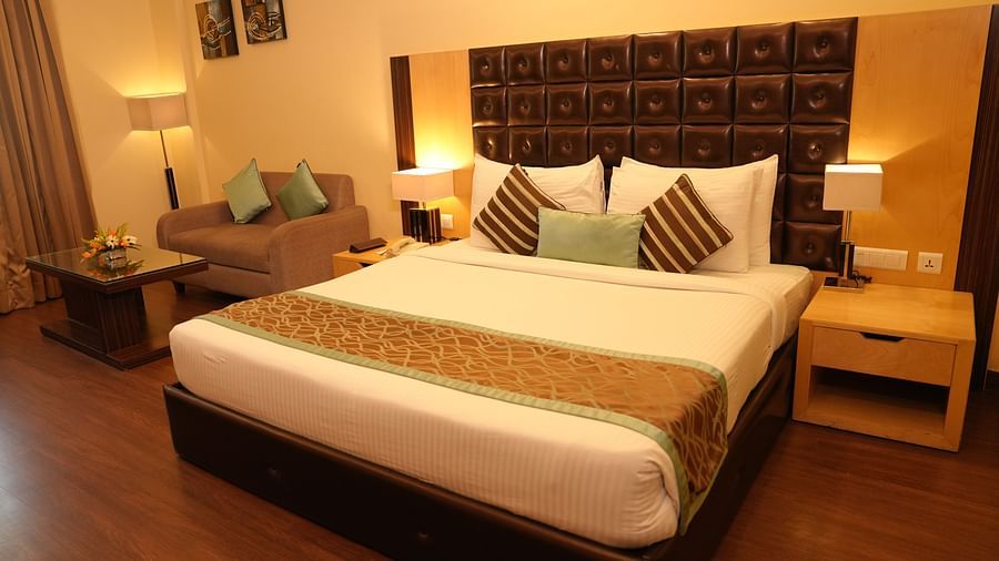 Hotel suite featuring a bed, seating area, desk, and a large window with curtains - Grand Plaza Lords Inn Jammu