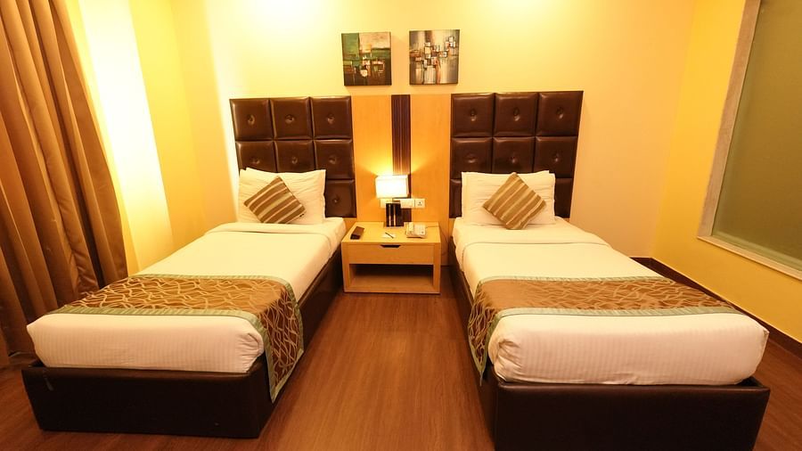 Hotel room with two beds, dark headboards, and beige curtains by the window - Grand Plaza Lords Inn Jammu