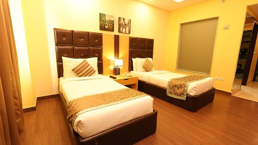 Hotel room with two beds, warm lighting, and dark wood headboards - Grand Plaza Lords Inn Jammu