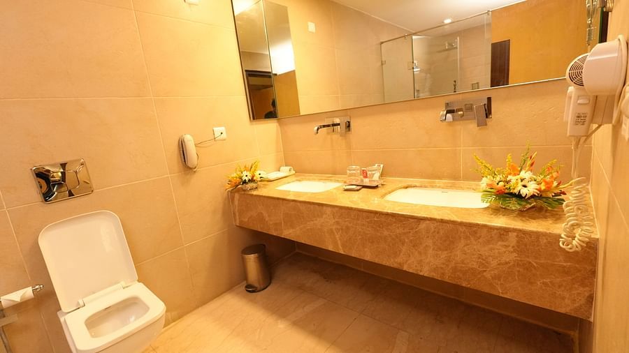 Bathroom with a marble countertop sink, toilet, and warm overhead lighting - Grand Plaza Lords Inn Jammu