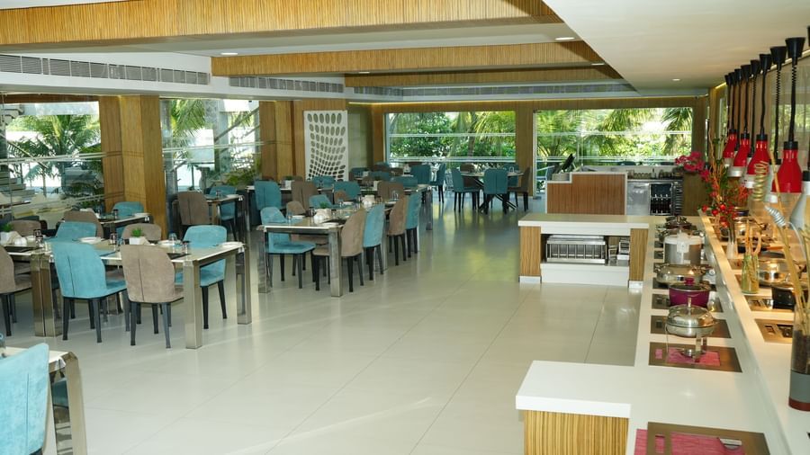 Restaurant seating area with rows of tables and blue chairs beside large windows at Grande Bay Resort & Spa.