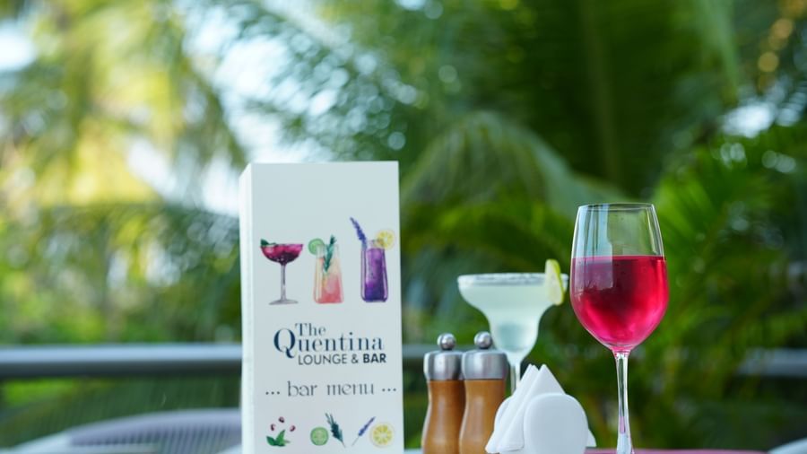 Outdoor table with a menu card, a red drink, a white drink and condiments at Grande Bay Resort & Spa.